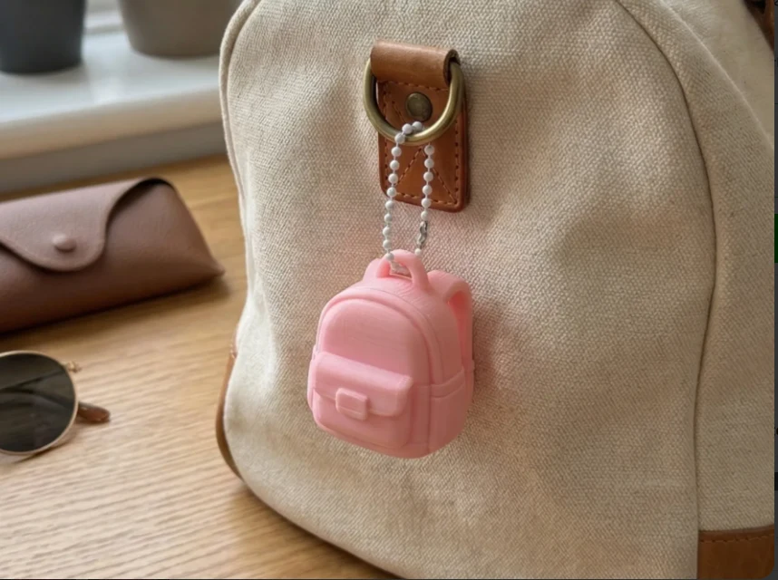 Mini Mochila rosa presa à alça de uma mochila, em cena ilustrativa de uso